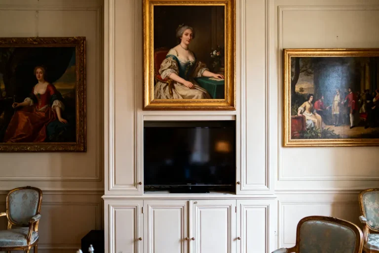 Salle décorée avec trois portraits anciens encadrés et une télévision moderne sous le tableau central.