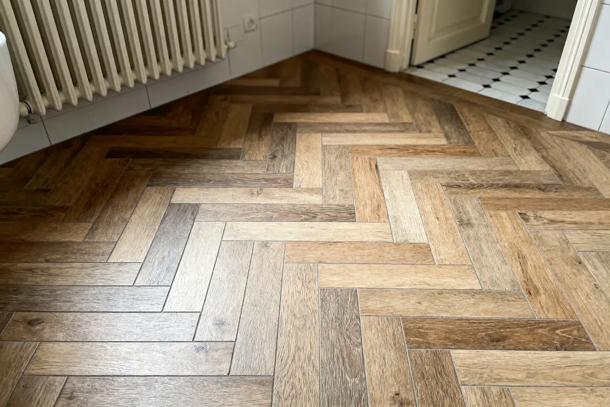 Parquet effet bois en chevrons dans une salle de bain avec carrelage noir et blanc au sol.