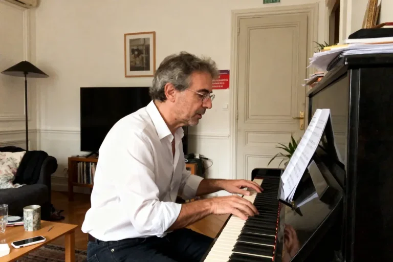 Un homme joue du piano, intérieur élégant, partitions posées, ambiance détendue et studieuse.