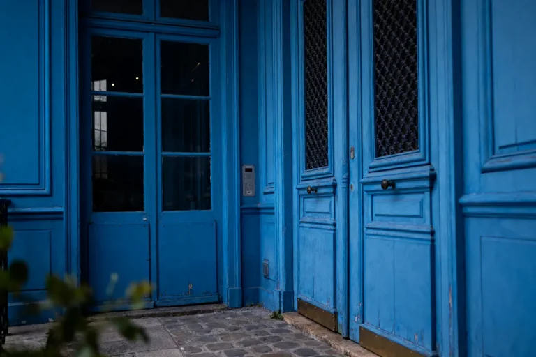 Porte bleue en bois avec fenêtres vitrées, sur un sol pavé, ambiance urbaine et tranquille.