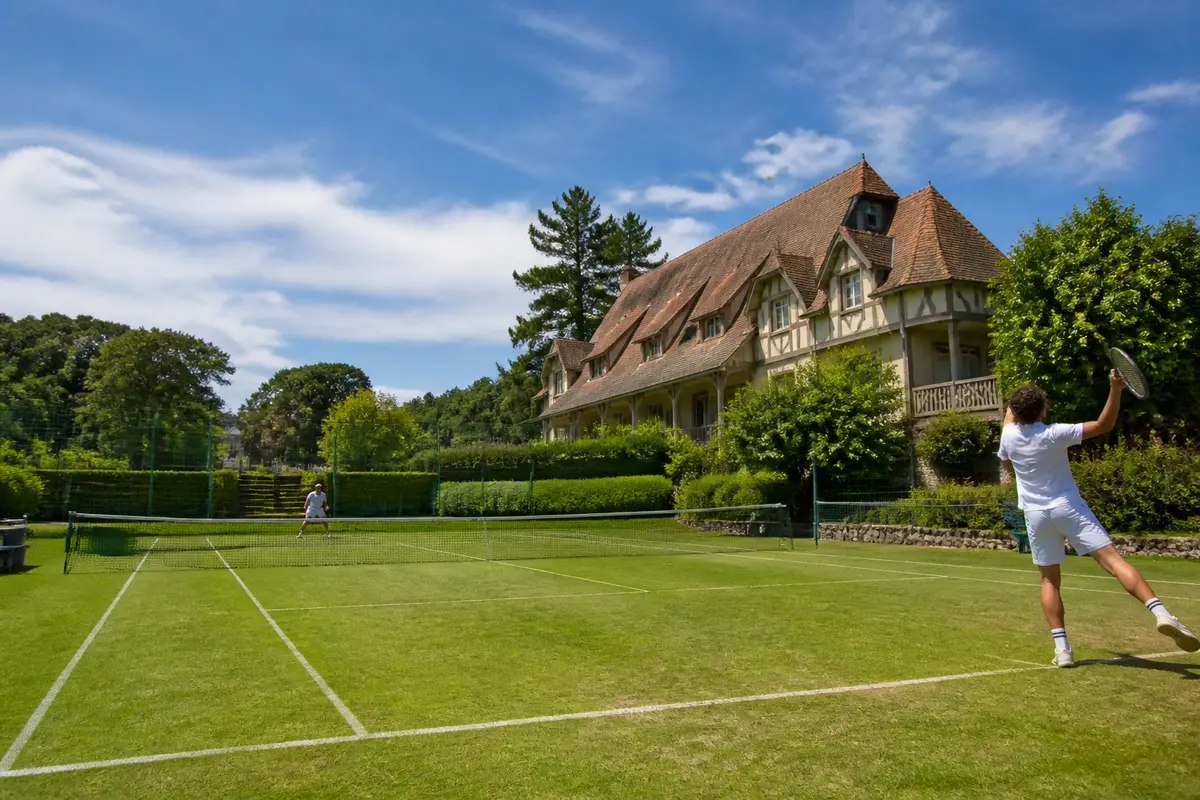 Joueurs de tennis sur gazon devant maison encadrée par l'Agence LTCDN.