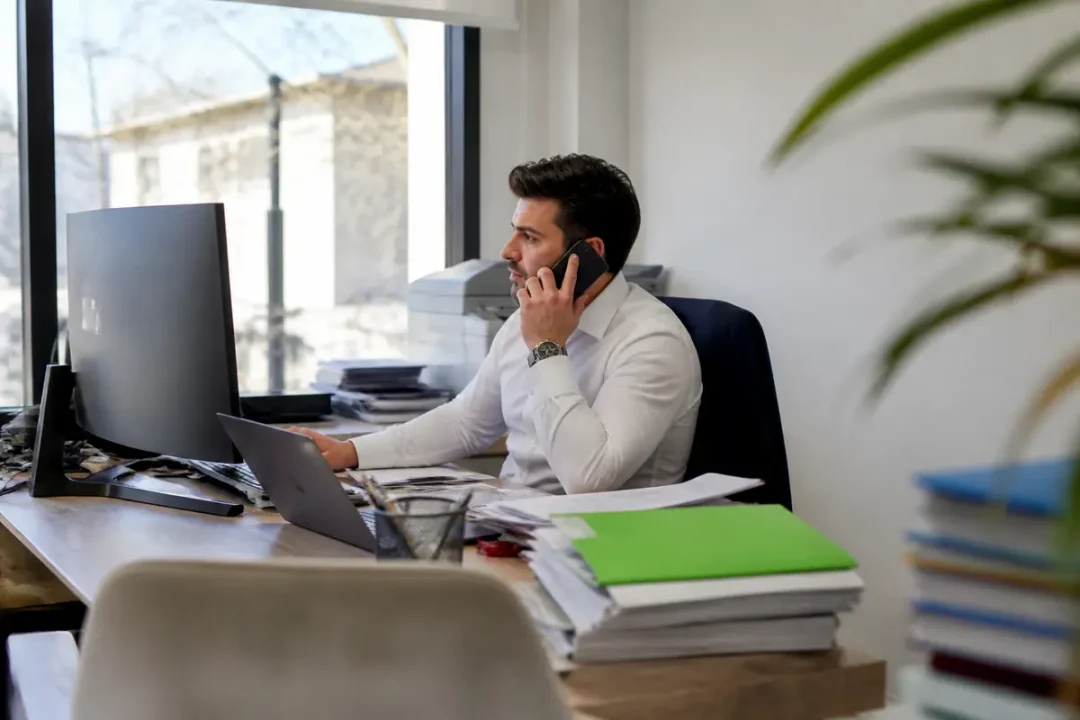 Un homme travaillant au bureau pour Artemis Courtage, téléphone à l'oreille et ordinateur portable.