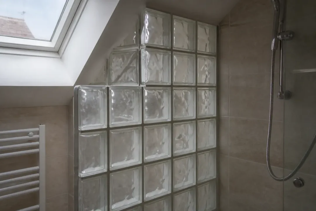Mur en carreaux de verre dans une salle de bain lumineuse avec douche et fenêtre.