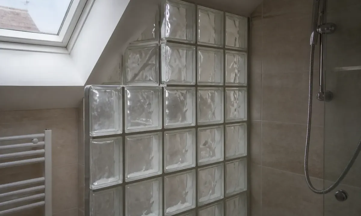 Mur en carreaux de verre dans une salle de bain lumineuse avec douche et fenêtre.