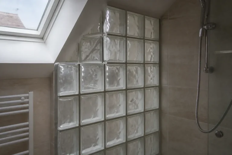 Mur en carreaux de verre dans une salle de bain lumineuse avec douche et fenêtre.